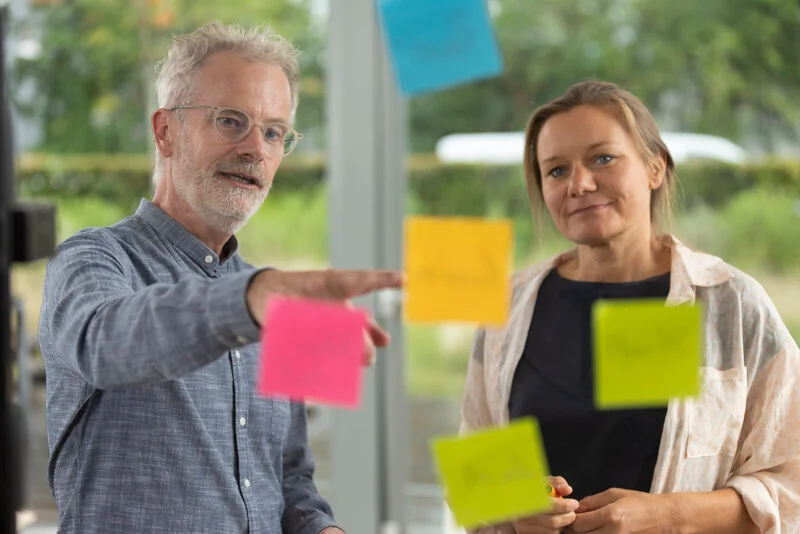 Coach und Coachee vor einer Glaswand mit Notizzetteln